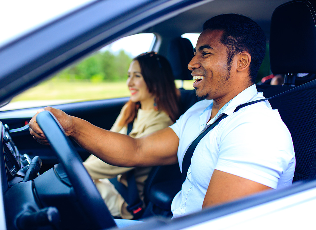 Insurance Solutions - Portrait of a Cheerful Young Man Driving in a Car with his Wife Sitting Next to Him on a Warm Day